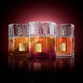 Lattafa Khamrah Dukhan by Lattafa 100ml EDP Unisex — Tiga botol minyak wangi Lattafa Khamrah dengan penutup kristal berfaset dan botol kaca gradien jingga ke merah, dipamerkan di atas permukaan hitam reflektif berlatar belakang gradien merah gelap.