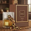 Lattafa Khamrah Qahwa by Lattafa 100ml EDP Unisex — Botol minyak wangi kaca jernih berisi cecair emas, tumpahan biji kopi, batang kayu manis, dan buah pelaga. Kotak coklat dengan rekaan geometri emas di latar belakang.