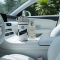 Lattafa Musk Mood by Lattafa 100ml EDP Unisex — A white and gold cylindrical box with a gold chain handle and a clear glass perfume bottle with a gold cap, placed on the white leather interior of a car.