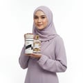 Lattafa Musk Mood by Lattafa 100ml EDP Unisex — Woman in a lilac hijab and dress holding a perfume bottle and its cylindrical box, both featuring gold accents and intricate patterns.
