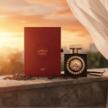 Lattafa Pride Nebras — Red textured box with gold Arabic script and 'NEBRAS' text, next to a black perfume bottle with a gold sunburst emblem and gold cap. Cocoa beans and vanilla pods are scattered around on a stone ledge.