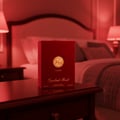 Lattafa Opulent Red by Lattafa 100ml Unisex — Red velvet perfume box with gold emblem and text, placed on a dark wooden nightstand next to a bed with red lamps.