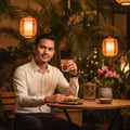 Lattafa Oud Lail Maleki by Lattafa 100 ml Unisex — Man in white shirt holding a drink, sitting at a table with a perfume bottle, snacks, and an orchid.