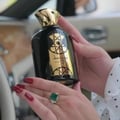 Lattafa Nasheet by Lattafa Perfume 100ml EDP Unisex — Black perfume bottle with gold cap and ornate gold label, held by hands with red nails, wearing an emerald ring.