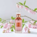 Lattafa Velvet Rose by Lattafa 100ml Unisex — Pink perfume bottle with rose gold accents and a crystal cap, set against a white background with delicate pink flowers and green leaves.