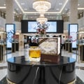 Lattafa Khalis Pure Oudi by Lattafa EDP 100ml — A gold-capped perfume bottle and its box sit on a black marble table in a well-lit luxury store, with a small spray bottle to the left.