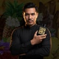Lattafa Qaed Al Fursan oleh Lattafa 90ml untuk Lelaki — Lelaki berbaju sut memegang botol minyak wangi hitam dan emas, dengan kotak sepadan di atas meja kayu.