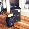 Lattafa Raghba for Men 100ml EDP — Black faceted perfume bottle with gold cap and matching box on a wooden surface.