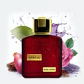 Lattafa Ramz Gold Lattafa Woman 100ml EDP — Red glass perfume bottle with gold cap, surrounded by a pink rose, apple, cinnamon sticks, and lavender sprigs, with purple liquid splashes.