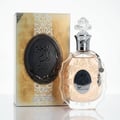 Lattafa Rouat Al Musk by Lattafa 100ml for Women — A clear glass perfume bottle with gold ornate details and a decorative charm, next to its matching gold and black patterned box.