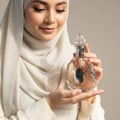 Lattafa Rouat Al Musk by Lattafa 100ml for Women — A woman in a white hijab holds a clear, ornate perfume bottle with a silver butterfly accent, looking down at it with a gentle smile.