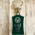 Lattafa Safeer by Lattafa Al Noble 100ml EDP — Green bottle with a gold deer head cap, featuring Arabic and English text and a deer logo on a light wooden background.