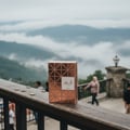 Lattafa Shahd by Lattafa Perfumes 100 ml Women — Rose gold geometric patterned perfume box sits on a wooden railing with a misty mountain landscape in the background.