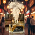 Lattafa Sheikh Al Shuyukh Concentrated by Lattafa 100ml — A clear glass perfume bottle with golden liquid, emitting white smoke, placed in front of its patterned box. The background shows a blurred night market with warm lights.