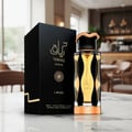 Lattafa Teriaq Intense by Lattafa 100ml Eau de Parfum — Black box with gold Arabic calligraphy and geometric pattern next to a clear glass perfume bottle with gold accents and amber liquid, set on a marble surface with a blurred cafe background.