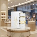 Lattafa Yara Moi by Lattafa 100ml EDP Women — White perfume bottle with gold ribbon detail and matching box on a marble pedestal, displayed in a luxury store setting.