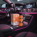 Lattafa Yara Tous by Lattafa 100ml EDP Women — Orange perfume bottle and box displayed on the center console of a luxury car with pink ambient lighting.