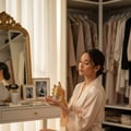 Maison Alhambra Anarch by Maison Alhambra 100ml EDP Women — Woman in a silk robe smelling a golden perfume bottle with a tassel, sitting at a vanity with makeup brushes and jewelry.