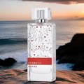 Maison Alhambra Aromatic Rouge by Maison Alhambra 100ml EDP — Clear glass perfume bottle with delicate floral vine pattern and a red label, set against a blurred ocean sunset background.