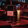 Maison Alhambra B.A.D. Femme by Maison Alhambra 100 ml — Perfume bottle and box displayed on a car's dashboard at night, with red ambient lighting.