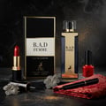 Maison Alhambra B.A.D. Femme Eau de Parfum — A black and gold perfume box, a gold-capped perfume bottle, red lipstick, and red nail polish arranged on a dark marble surface with gold glitter.
