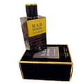 Maison Alhambra B.A.D. Homme Eau de Parfum — A black and gold perfume bottle with a textured black cap and gold accents, placed on its matching black velvet box with gold trim.
