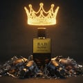 Maison Alhambra B.A.D. Homme Eau de Parfum — A golden crown hovers above a glass perfume bottle surrounded by shattered glass fragments and broken bottles.