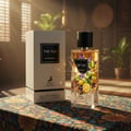 Maison Alhambra The Tux by Maison Alhambra 90ml EDP for Men — A white perfume box and a clear glass bottle of The Tux perfume, featuring citrus and floral elements, are displayed on a patterned fabric surface with sparkling light effects.