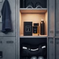 Maison Alhambra Dark Door Intense by Maison Alhambra 100ml Men — Black perfume box and bottle with gold accents, placed on a shelf in a locker room with a towel and sneakers.