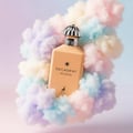 Maison Alhambra Decadent Wonder Her EDP 100 ml Alhambra — Peach-colored perfume bottle with a silver fluted cap, surrounded by pastel-colored cotton candy clouds against a gradient background.