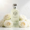 Maison Alhambra Delilah Blanc — Frosted glass perfume bottle with silver ornate cap, surrounded by white roses and gold glitter on a white background.