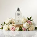 Maison Alhambra Delilah Blanc by Maison Alhambra 100ml EDP — Frosted glass bottle with silver cap, presented on a gold pedestal surrounded by a lush arrangement of white and pink roses and baby's breath.