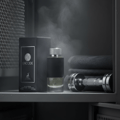 Maison Alhambra Encode By Maison Alhambra 100ml for Man — Black textured perfume bottle with silver cap, next to its box, on a shelf with dumbbells and folded towels, gym locker background.