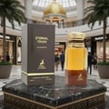 Maison Alhambra Eternal Touch — A dark brown box and a golden-capped perfume bottle displayed on a marble pedestal in a mall atrium with palm trees and shoppers in the background.
