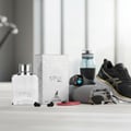 Maison Alhambra Expose Blanc by Maison Alhambra 100ml EDP Men — White perfume bottle and silver patterned box with a deer logo, next to a smartwatch, water bottle, running shoes, sunglasses, and a rolled towel.