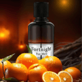 Maison Alhambra Fortnight by Maison Alhambra 100ml EDP Men — A dark glass perfume bottle with a black cap, labeled 'Fortnight For Men', surrounded by fresh, dewy oranges and leaves against a warm, blurred background.