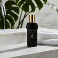 Maison Alhambra Glacier Le Noir — Black perfume bottle with gold cap, set on a marble countertop with running water from a faucet and folded white towels.