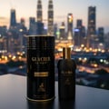 Maison Alhambra Glacier Le Noir — Black perfume bottle and cylindrical box with gold accents, set against a blurred city skyline at dusk.