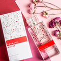 Maison Alhambra Aromatic Rouge by Maison Alhambra 100ml EDP — A clear glass perfume bottle with a floral design and a red label, next to its white box with matching design. Dried roses are scattered around.