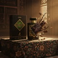 Maison Alhambra Infini Oud Joyous — Black perfume box and bottle with oud wood pieces exploding outwards, set on a patterned cloth.