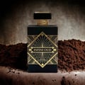 Maison Alhambra Infini Oud by Maison Alhambra Man 100ml EDP — Black bottle with gold geometric design and cap, placed on a surface with dark brown powder or soil.