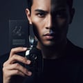 Maison Alhambra Hercules by Maison Alhambra For Him 100ml — Man holding a black perfume bottle and its matching box, with dramatic lighting casting a shadow across his face.