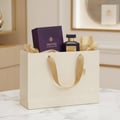 Maison Alhambra Infini Intoxicating Cherry — A purple box and dark glass perfume bottle with gold accents sit inside a cream-colored gift bag with gold ribbon handles, tissue paper visible.