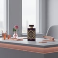 Maison Alhambra Infini Rose by Maison Alhambra 100ml EDP Unisex — Botol minyak wangi ungu gelap dengan rekaan geometri emas dan penutup, diletakkan di atas meja bersama bunga ros merah jambu dalam pasu kecil, pemegang pen emas ros, dan stapler emas ros.