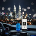 Maison Alhambra Jean Lowe Azure by Maison Alhambra EDP 100 ml — Blue perfume bottle and cylindrical box on a car dashboard at night with city skyline and Petronas Twin Towers in the background.