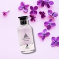 Maison Alhambra Jean Lowe Matiere by Maison Alhambra 100ml — Clear glass perfume bottle with black cap, surrounded by purple lilac flowers on a pink background.