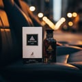 Maison Alhambra Jean Lowe Noir — A dark glass perfume bottle and its white box packaging are placed on a dark leather surface, with blurred city lights in the background.
