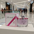 Maison Alhambra Just Married by Maison Alhambra Woman 100ml — A white box with pink ribbon detail and a clear glass perfume bottle with pink liquid and a silver cap, displayed in a mall.