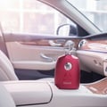 Maison Alhambra Kalos by Maison Alhambra Woman 100ml — Red perfume bottle with silver cap, placed on the leather armrest of a car interior.