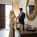 Maison Alhambra Karat by Maison Alhambra 100ml EDP — Couple in formal wear preparing to go out, with perfume bottle and accessories on a table in the foreground.